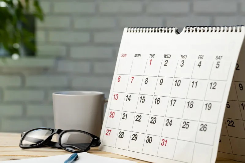 Wall calendar on a desk beside a coffee mug and reading glasses